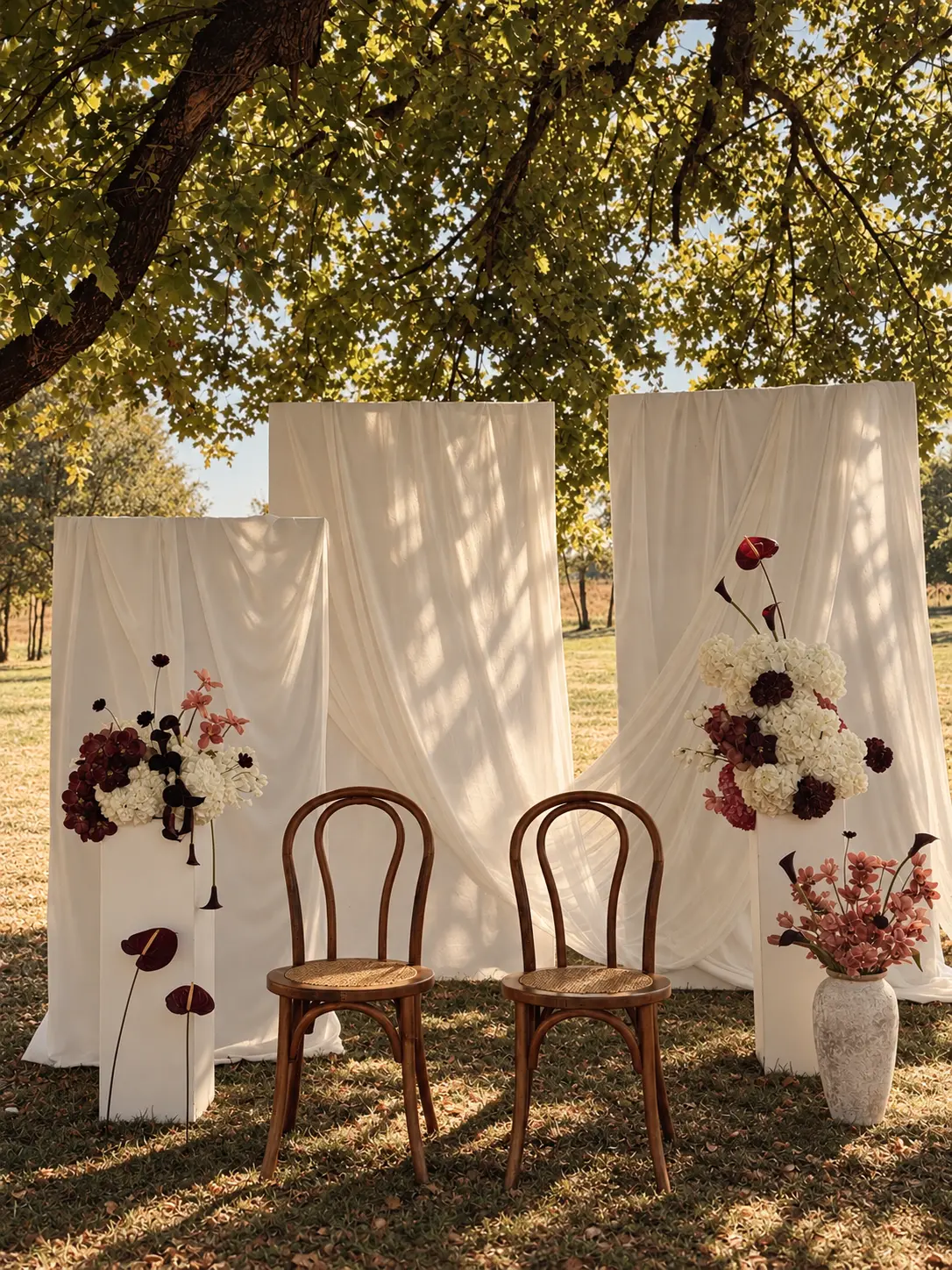 Mise en scène florale en extérieur : chaises en bois, voilages blancs et compositions bordeaux et blanches