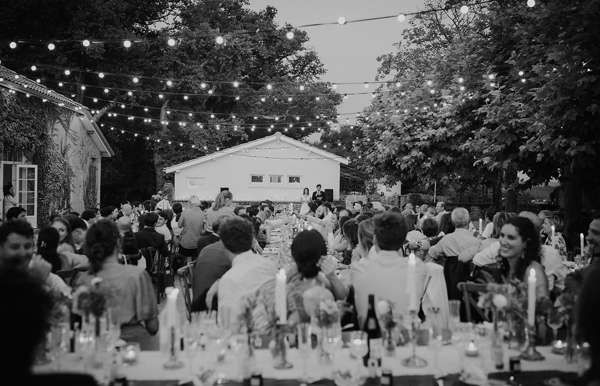 Grande tablée de mariage en plein air sous les guirlandes lumineuses, en noir et blanc